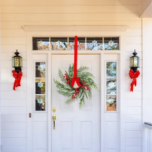 Close-up of artificial pine wreath with red berries and bow hanging on white wooden door