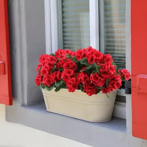 Géraniums artificiels rouges dans une jardinière crème sur un rebord de fenêtre