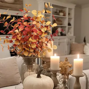 Artificial fall eucalyptus stems in orange and red tones placed in a clear glass vase
