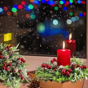 Détail d'une couronne de Noël enneigée avec baies rouges, pommes de pin et bougie pilier