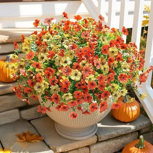Outdoor autumn decor featuring artificial orange and yellow flowers in a white striped pot