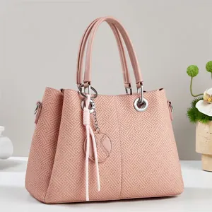 Detail of pink handbag featuring embossed geometric texture and soft tassel charm pendant