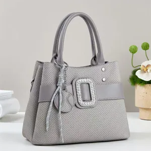 Detail of dark gray handbag featuring geometric embossing and a large rhinestone buckle