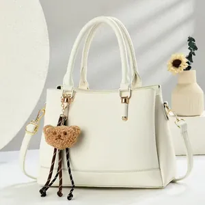 Close-up of beige lychee texture handbag with brown bear charm and gold hardware