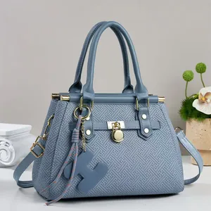 Blue-grey embossed tote bag with gold hardware and tassel charm on a studio background