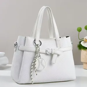 Close-up of white embossed tote bag with woven texture, decorative buckle and striped charm
