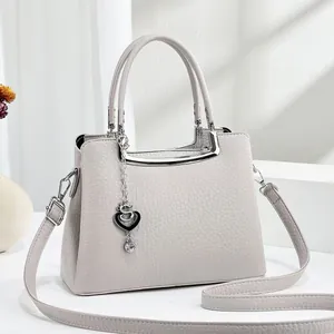 Détail d'un sac à main gris clair texture litchi avec ferrures argentées et pendentif cœur