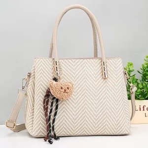 Beige woven tote bag with brown plush bear charm and adjustable shoulder strap