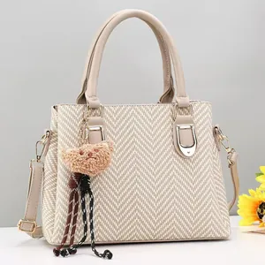 Beige woven texture handbag with shoulder strap and plush bear charm on grey background