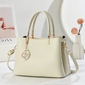 Détail d'un sac à main beige texture litchi avec dorures et pendentif fleur dorée