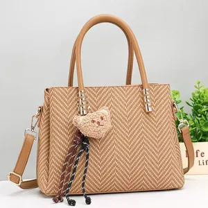 Detail view of khaki woven tote bag with detachable strap and plush bear pendant