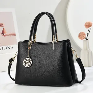 Détail du sac à main en cuir noir avec ferrures dorées et pendentif fleur ajouré