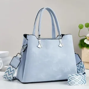 Detail der hellblauen Nubuk-Handtasche mit silbernen Anhängern und breitem Schultergurt