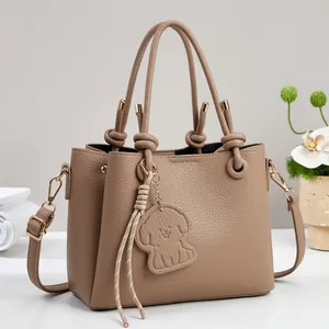 Light brown pebble leather handbag with dog charm and gold hardware on white surface