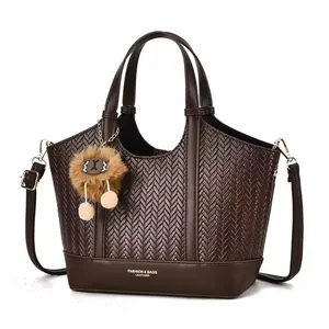 Brown woven tote bag with smooth leather handles and a plush pompom pendant on white background