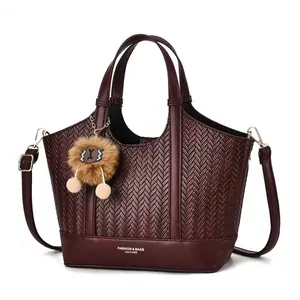 Detail of dark red woven tote bag with smooth leather trim and plush pom-pom charm