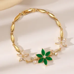 Detailaufnahme eines vergoldeten Blumenarmbands mit grünen und weißen Zirkonia-Steinen