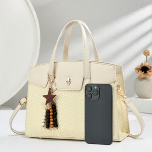 Detail of woven handbag with heart lock, tassels and smartphone for size reference