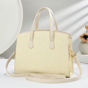 Detail of straw-textured tote bag with light beige handles and gold metal buckles