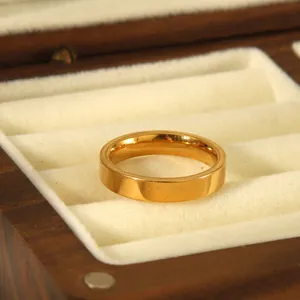 Minimalist 4mm gold stainless steel band ring with polished mirror finish on wood display