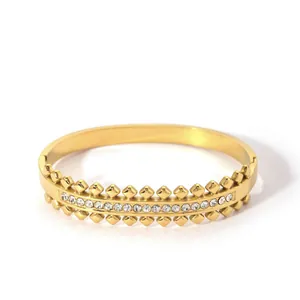 Close-up of gold stainless steel bangle with diamond-set accents and rivet textures