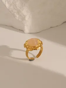 Detail of pink natural stone ring with gold petal setting on white rock background