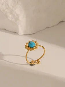 Gros plan sur bague en acier inoxydable doré avec pierre turquoise et base en rayon de soleil