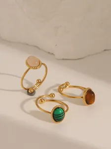 Dettaglio di tre anelli regolabili in oro con pietre di quarzo, malachite e occhio di tigre