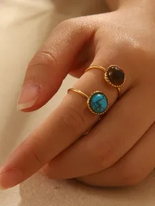 Detailed macro view of two adjustable gold-tone rings with inset round turquoise and tiger eye stones