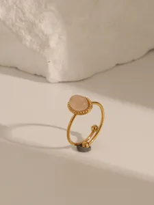 Dettaglio anello regolabile dorato con pietra rosa ovale e bordo perlato su pietra