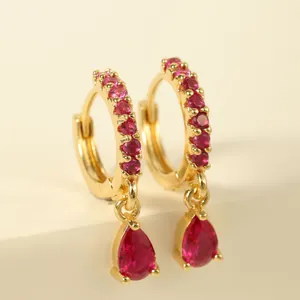 Detail view of gold hoop earrings featuring round and teardrop red gemstones on white base