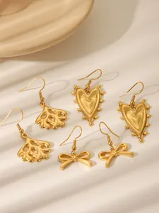 Detailliertes Set aus drei goldenen Ohrringen mit Herz-, Korallen- und Schleifendesigns auf Tablett