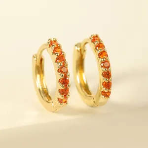 Macro shot of gold huggie earrings featuring a pavé setting with bright orange gemstones
