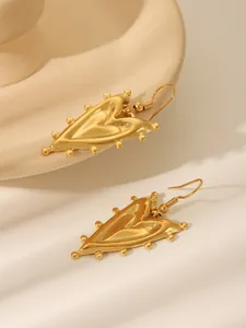 Detail von goldenen Herzohrringen mit gerippter Textur und Perlenrand auf Keramik