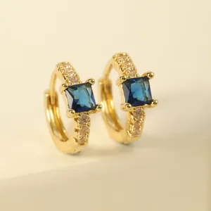 Macro view of gold-plated huggie earrings with square blue sapphire and white crystals