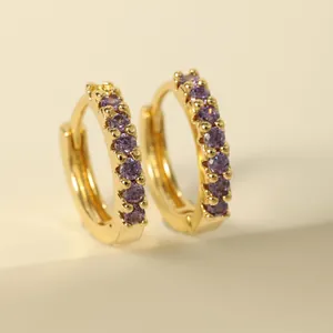 Detailed close-up of golden huggie earrings with sparkling purple zircon stones