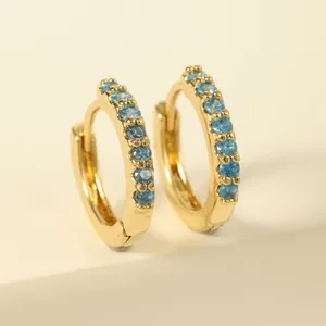 Macro view of gold huggie earrings featuring round-cut sky blue gemstones inlay