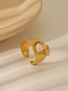 Detailed close-up of textured gold band ring with pearl and heart charms