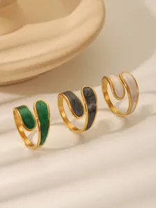 Detail of vintage gold rings with green, grey, and white enamel inlay under natural light