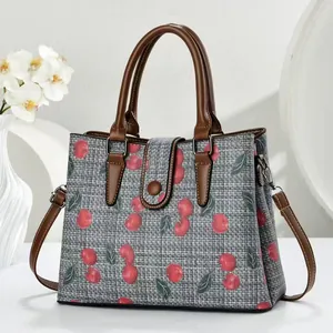 Gray canvas tote bag with cherry print and brown leather straps in a minimalist setting