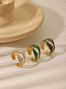 Set of irregular gold rings with white, green and black enamel details on beige base
