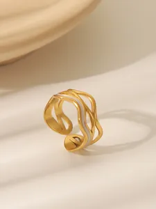 Macro detail of wave layered golden ring with white enamel accents on a textured tray