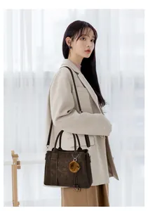 Détail d'un grand sac cabas marron foncé avec pompon porté sur un manteau