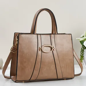 Brown leather handbag with gold oval buckle and detachable shoulder strap in a studio setting