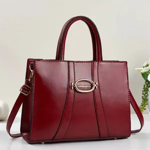 Detail view of burgundy leather handbag showing polished surface and metallic oval buckle