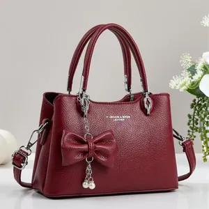 Detail of wine red litchi texture leather handbag with pearl and bow charm decorations
