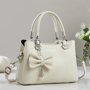 Detail der cremeweißen Handtasche mit Litschi-Muster, großer Schleife und Perlenkette