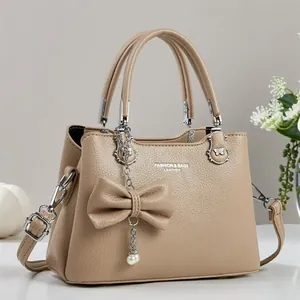 Details der khakifarbenen Handtasche mit Kieseltextur, Schleifenanhänger und Silberbeschlägen