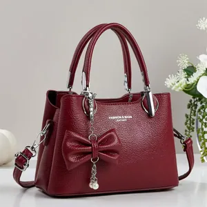 Detail of burgundy lychee leather handbag with decorative bow and pearl pendant charm