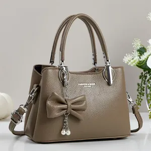 Detail of brown litchi pattern leather handbag with pearl bow charm and metal buckle